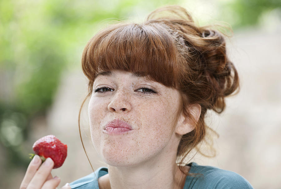 Germany, Berlin, Close up of young woman eating strawberry, smiling, portrait Photograph by Westend61