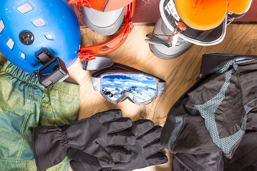 Getting ready for winter vacation. Set of snowboard equipment on the wooden floor. Goggles, snowboard, jacket, boots, gloves, suitcase Photograph by Artursfoto