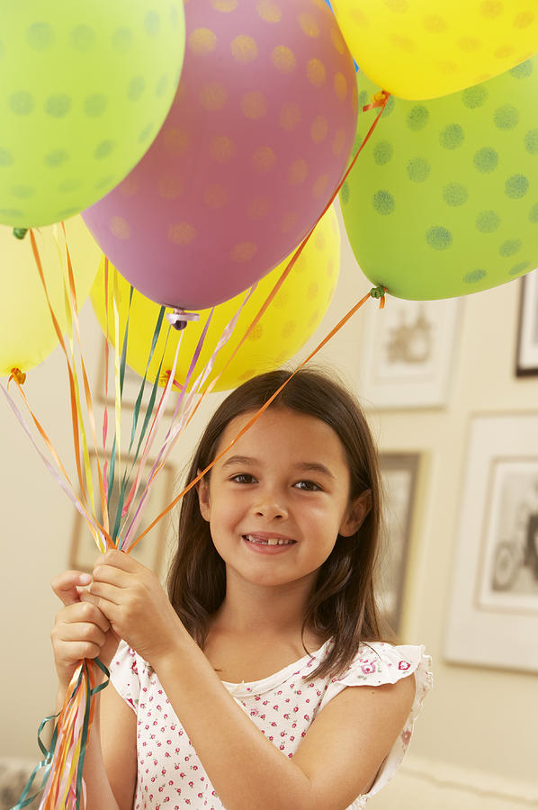Girl (5-7) holding bunch of helium balloons, smiling, portrait Photograph by Andrew Olney