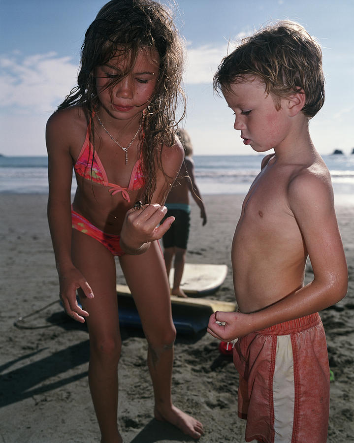 Girl (8-10) showing boy (4-6) crab on beach Photograph by Kevin Hatt