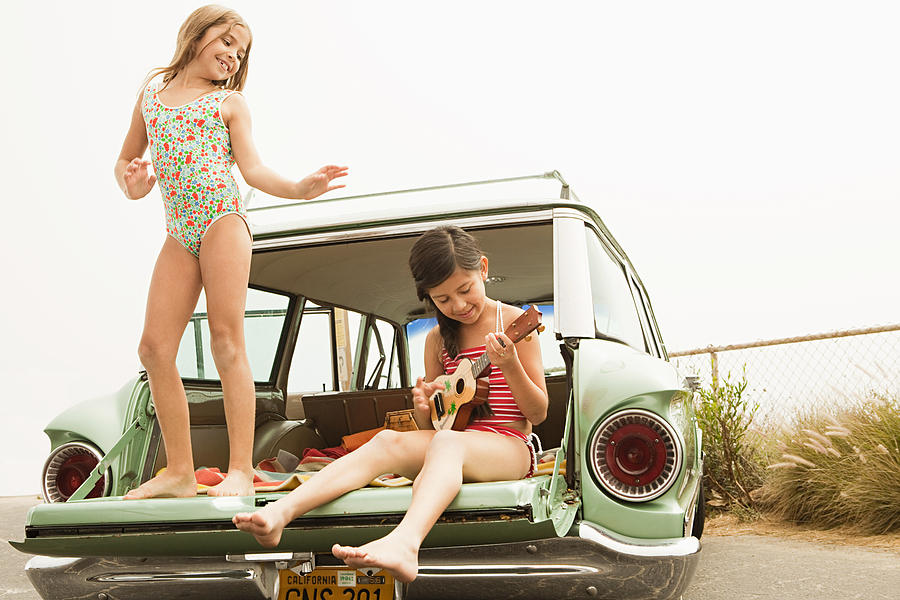 Girl dancing on car boot, another girl playing guitar Photograph by Image Source