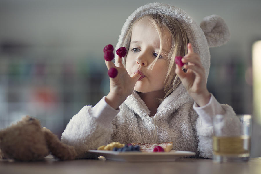 Girl in cozy hooded pyjamas, eating raspberries off her fingers Photograph by Elva Etienne
