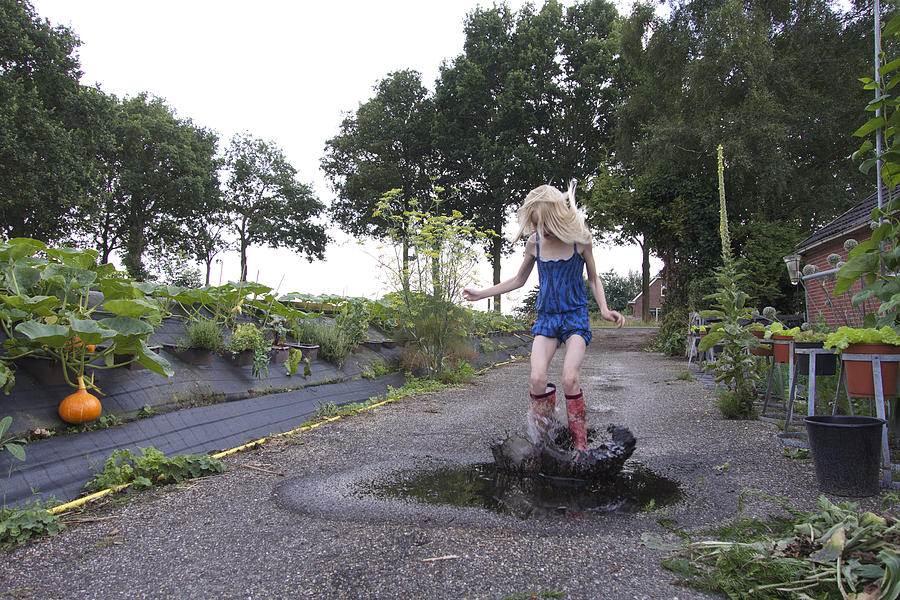 Girl jumping in muddy puddle in driveway Photograph by Lucy Lambriex