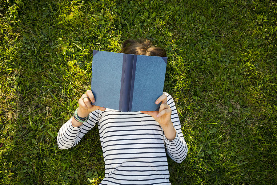 Girl lying on meadow reading a book Photograph by Westend61