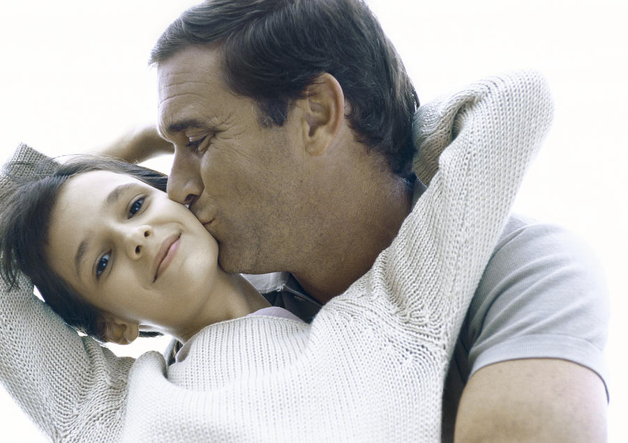 Girl reaching arms back around fathers neck, father kissing girls cheek Photograph by Laurence Mouton