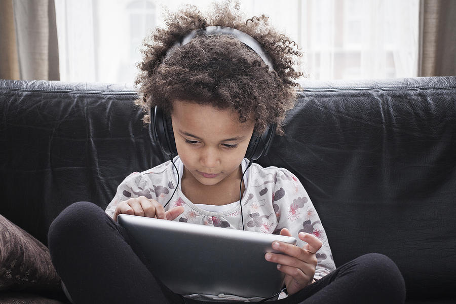 Girl sitting on sofa using digital tablet and headphones Photograph by Tom Odulate