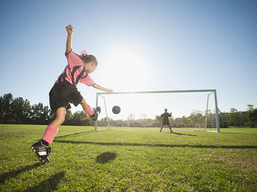 Girl soccer player kicking soccer ball at net Photograph by Blend Images - Erik Isakson