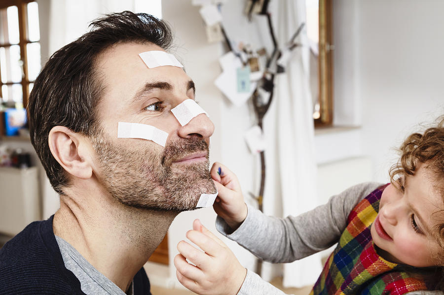 Girl sticking adhesive plaster onto fathers chin Photograph by Sporrer/Rupp