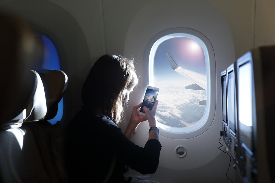 Girl taking photo out of airplane window Photograph by Peter Cade
