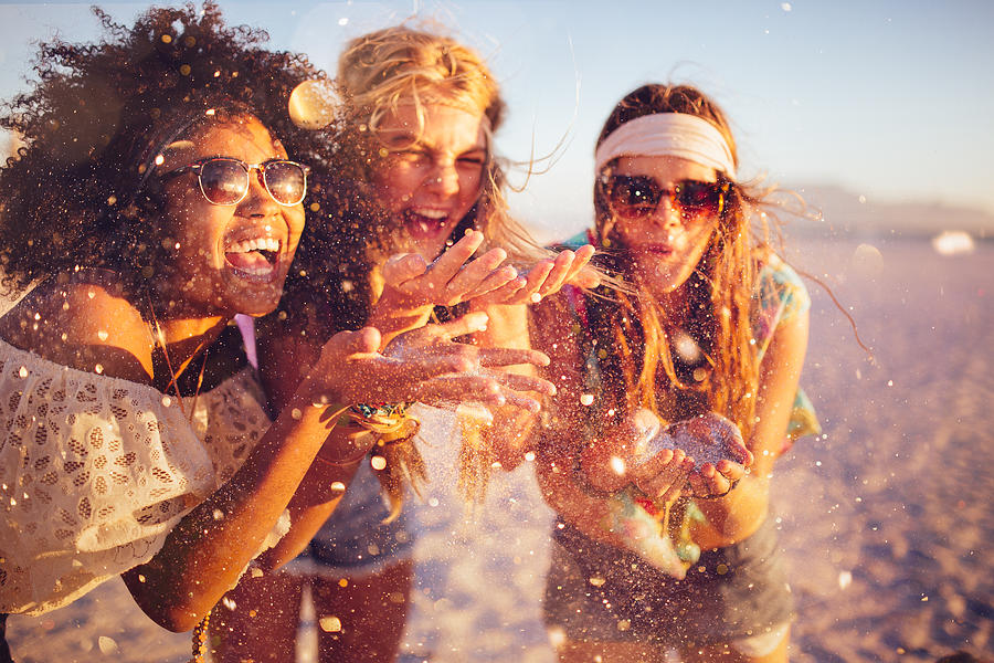Girls blowing confetti from their hands on a beach Photograph by Wundervisuals