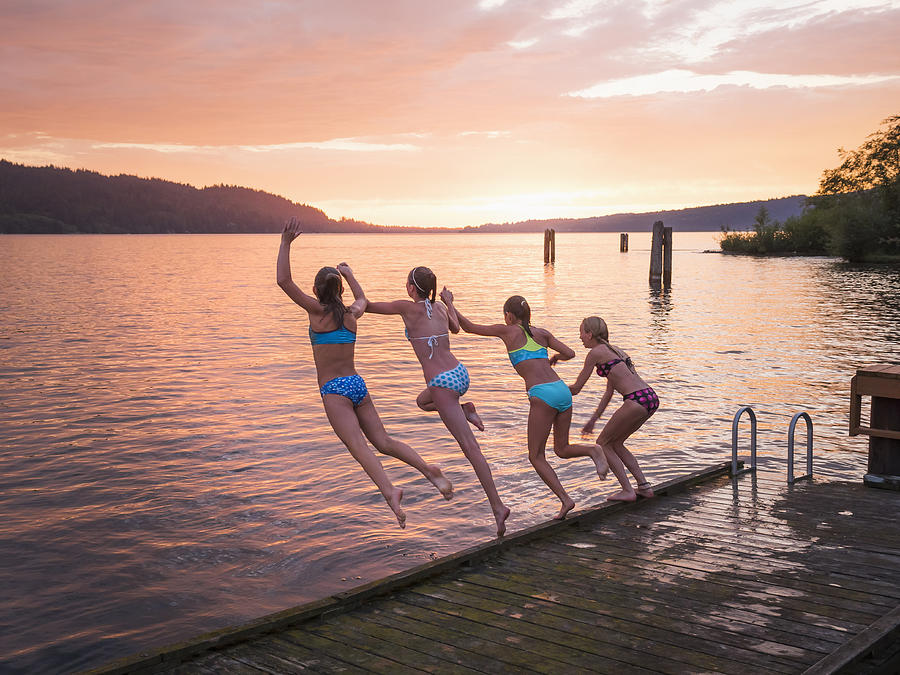 Girls jumping into lake from wooden dock Photograph by Don Mason