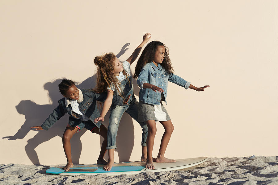 Girls playing on surfboard on the beach, on studio backdrop Photograph by Klaus Vedfelt