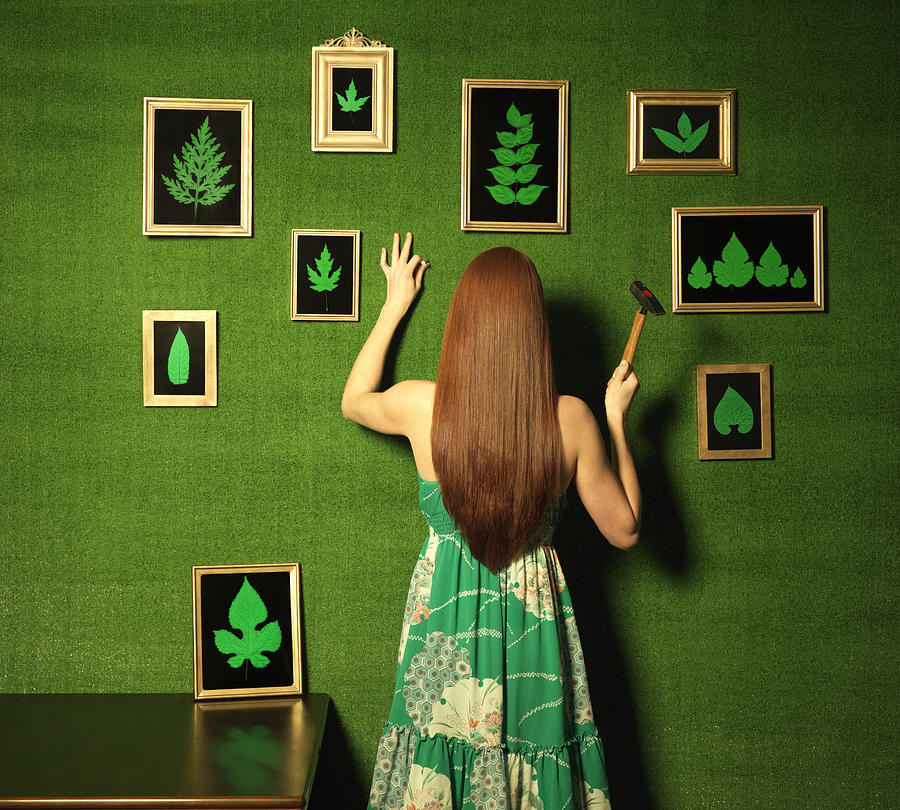Green room with a woman hanging pictures of leaves on the wall. Photograph by Henrik Sorensen