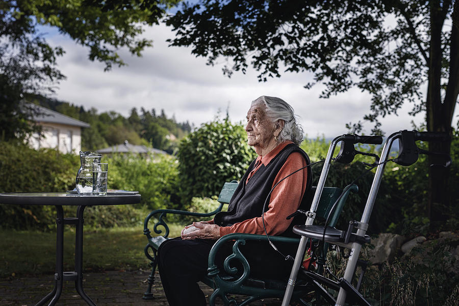 Großmutter mit Rollator sitzt auf Parkbank Photograph by Martin Steinthaler