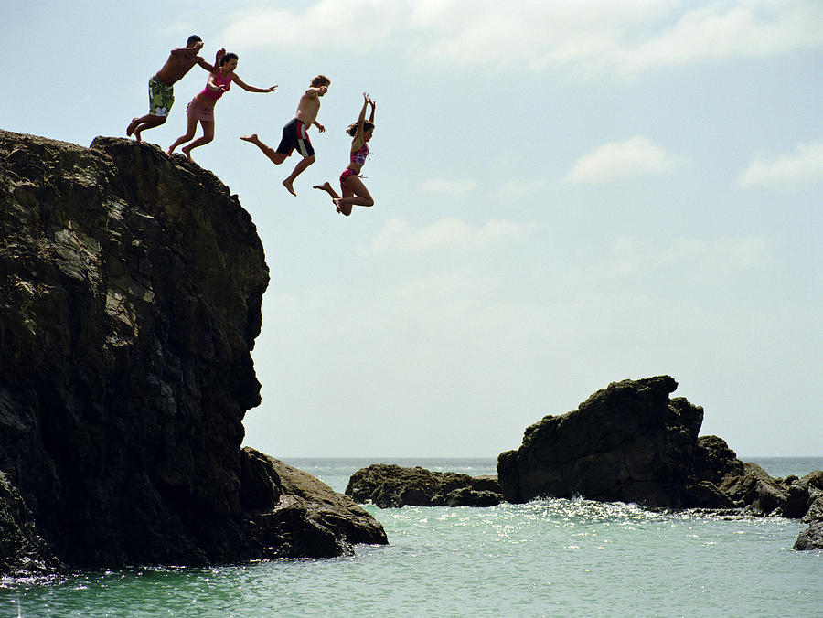 Group of friends jumping into ocean from rock cliff Photograph by Mike Powell