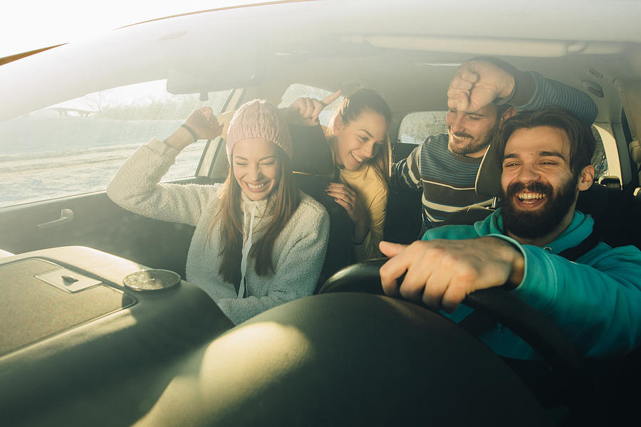 Group of happy friends having fun while dancing during a road trip in the car. Photograph by Skynesher