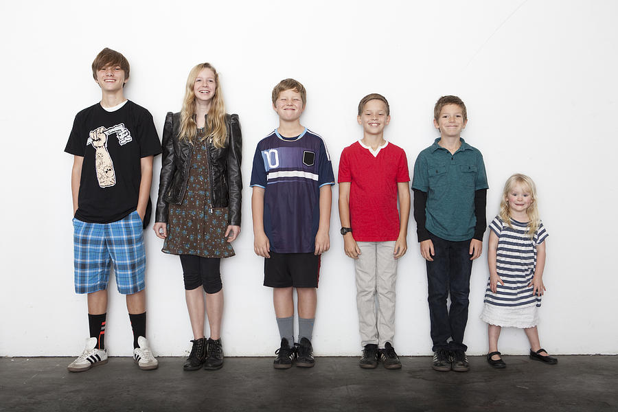 Group of sibling in line against white wall Photograph by Sean Murphy