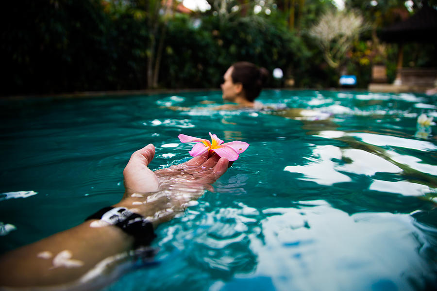 Guy holding from personal perspective a beautiful flower while swimming with girl in the Bali island during travel vacations in Indonesia. Photograph by Artur Debat