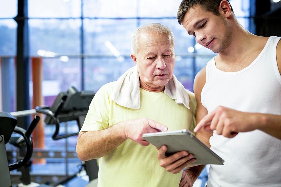 Gym Trainer Showing Tablet To Senior Man Photograph by Science Photo Library