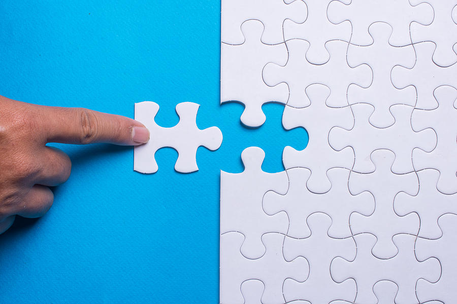 Hand holding piece of white puzzle on blue background. Business and team work concept. Photograph by Azri Suratmin