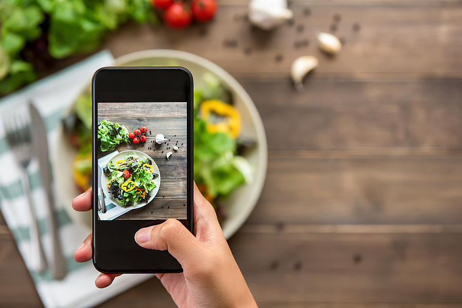 Hand holding smartphone taking photo of beautiful food, mix fresh green salad Photograph by Kritchanut