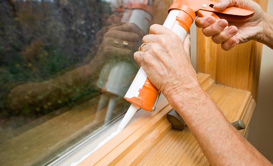 Hands Applying Weather Seal Caulk to Window Frame Photograph by BanksPhotos