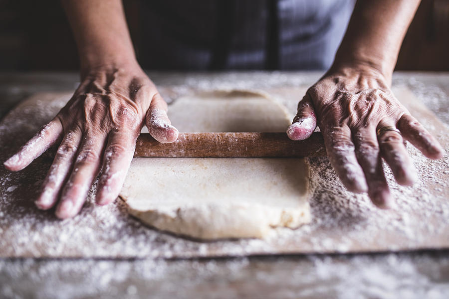 Hands baking dough with rolling pin on wooden table Photograph by Anchiy