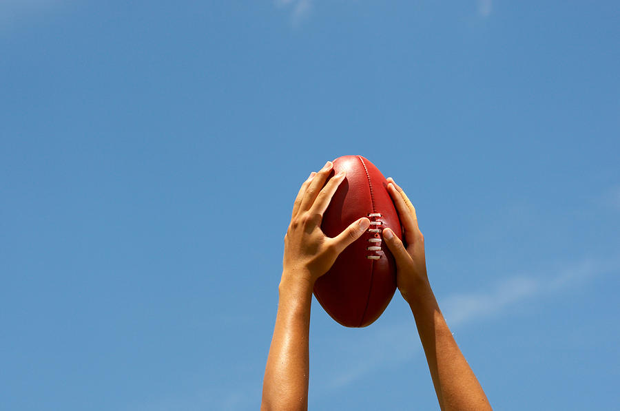 Hands holding Australian football up to the sky Photograph by Cameron Spencer