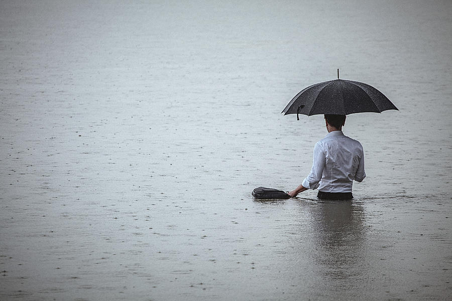 Handsome man standing in water and holding umbrella during rain Photograph by Gruizza