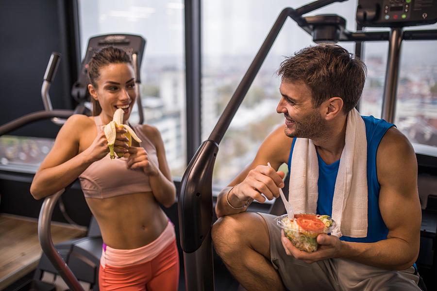 Happy athletic couple eating healthy food on a break in a gym. Photograph by Skynesher
