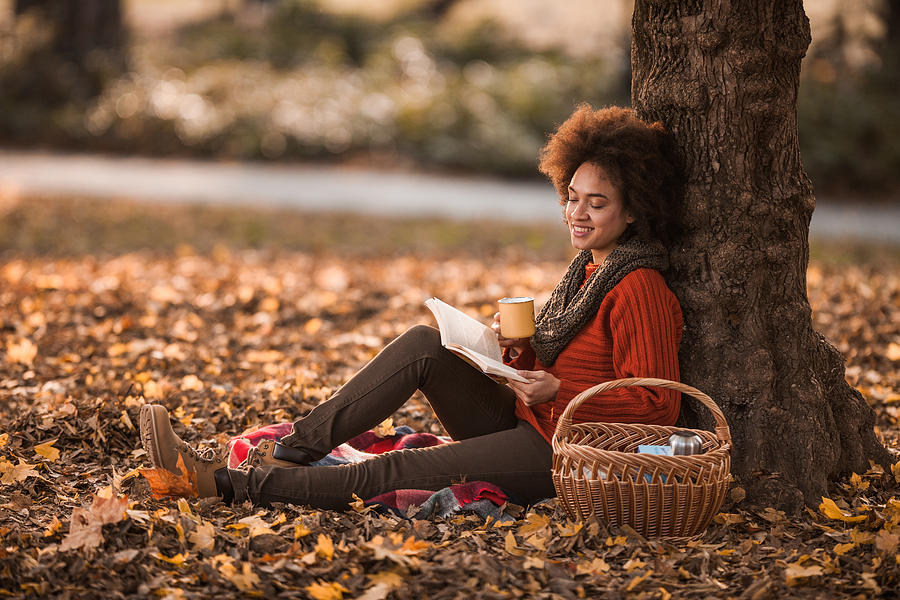 Happy black woman reading a book while enjoying on picnic in autumn day. Photograph by Skynesher