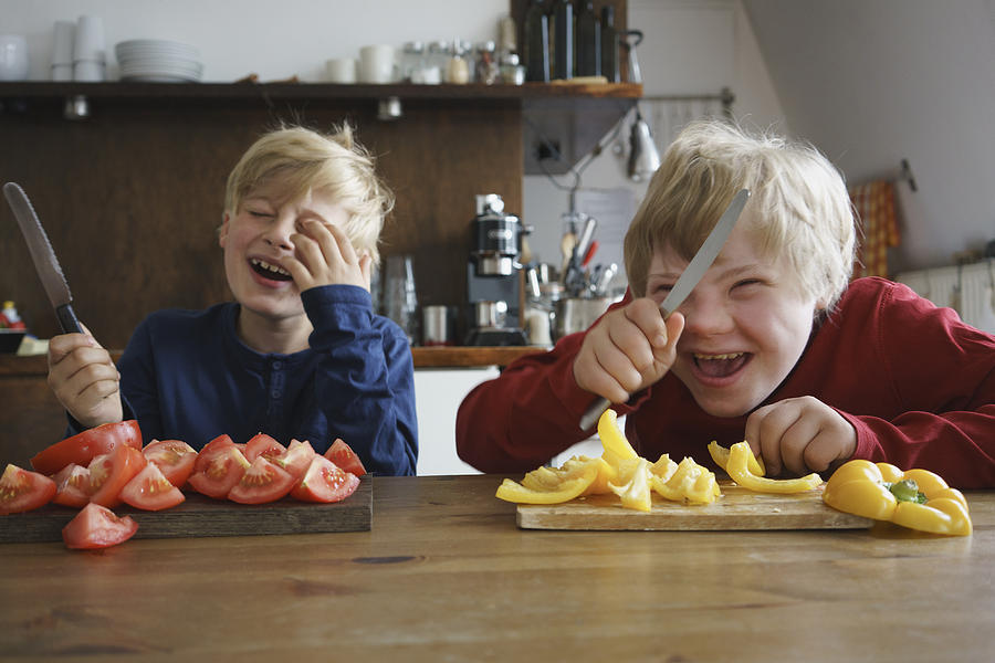 Happy brothers holding knives at table with vegetables in kitchen Photograph by Halfdark