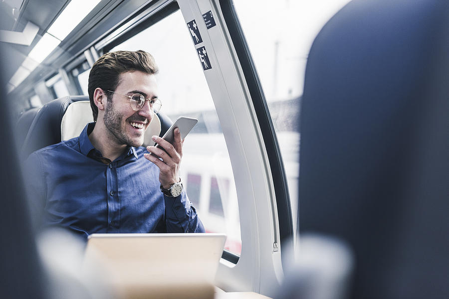 Happy businessman in train using cell phone Photograph by Westend61