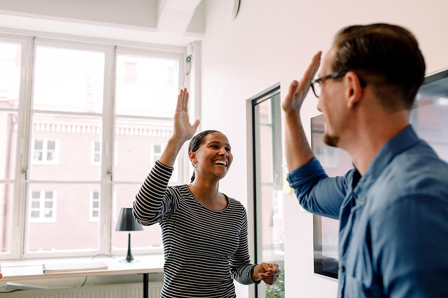 Happy businesswoman giving high-five to male colleague in office Photograph by Maskot