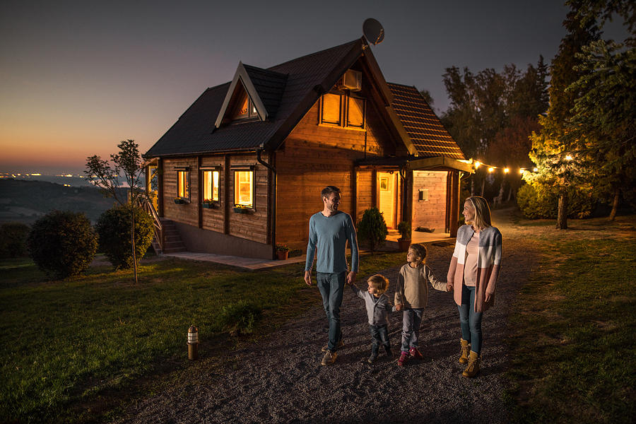 Happy family holding hands and walking by their chalet in the evening. Photograph by Skynesher