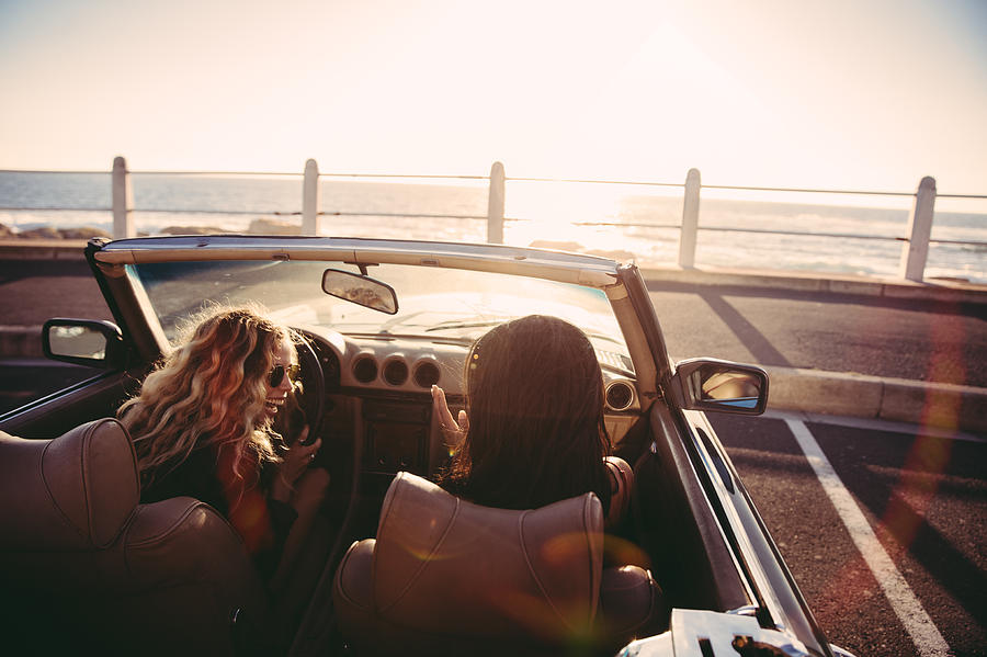 Happy female friends cheering in a convertible at sunset Photograph by Wundervisuals