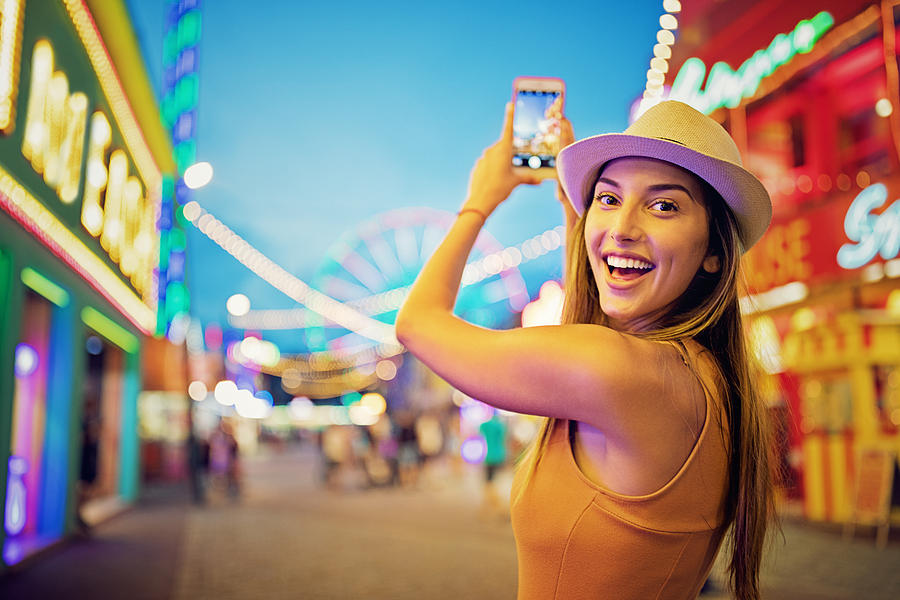 Happy girl is taking pictures with her mobile phone in a funfair Photograph by Praetorianphoto