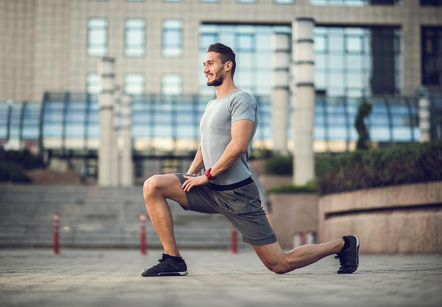 Happy male athlete exercising lunges on the city street. Photograph by BraunS