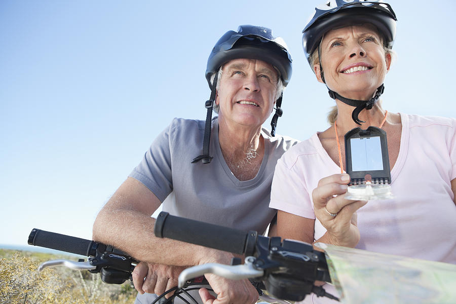 Happy mature woman mountain biking with man using GPS Photograph by OJO Images