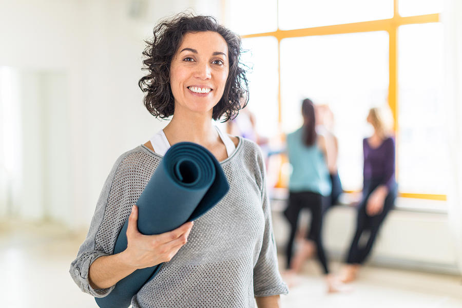 Happy mature woman with a yoga mat in health club Photograph by Alvarez