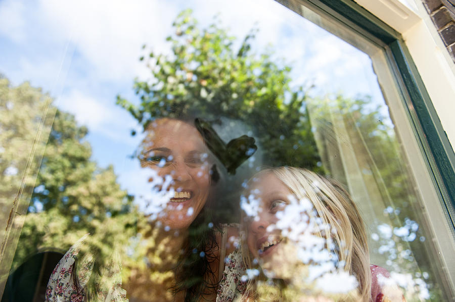 Happy mother and daughter with heart on window Photograph by Lucy Lambriex