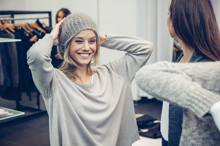 Happy oung woman putting on woolly hat in a boutique Photograph by Westend61