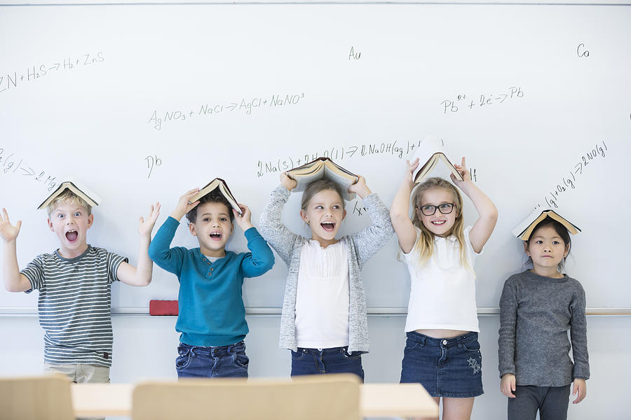 Happy pupils with books above their heads standing at whiteboard with formulas in class Photograph by Westend61