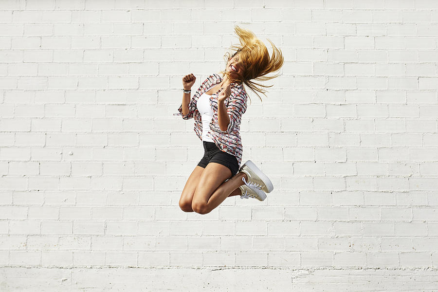 Happy young woman jumping mid-air in front of white wall Photograph by Westend61