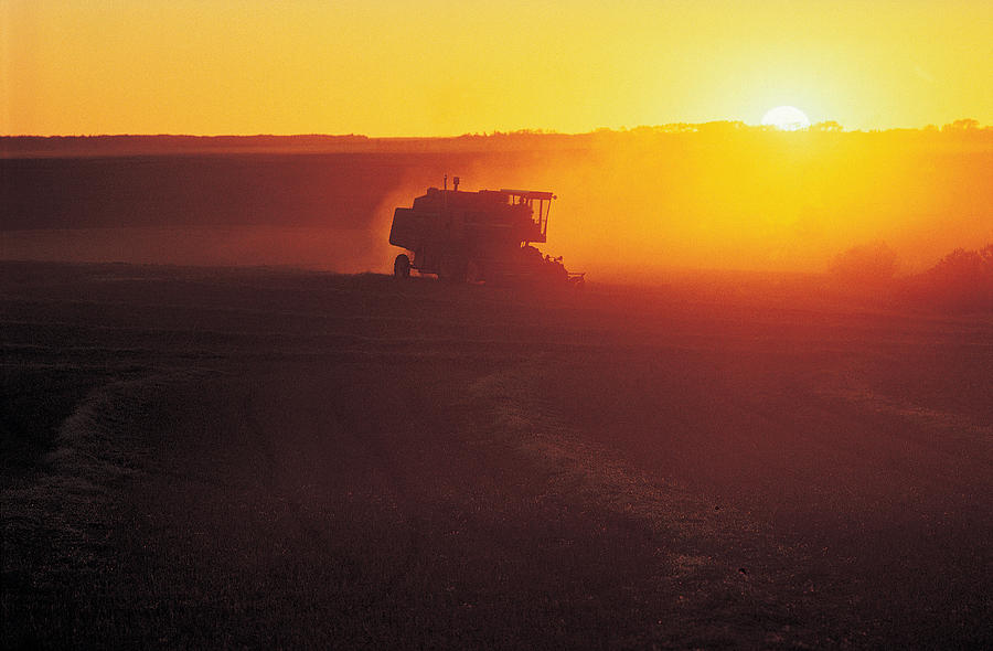 Harvester in field at sunset Photograph by Digital Vision.