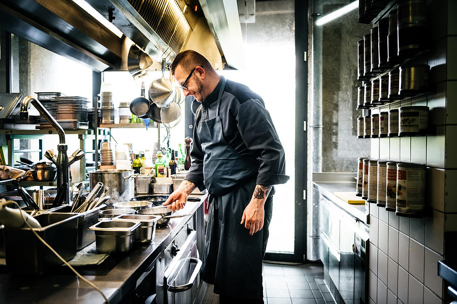 Head Chef Cooking On Hob In Well Stocked Restaurant Kitchen Photograph by Tom Werner
