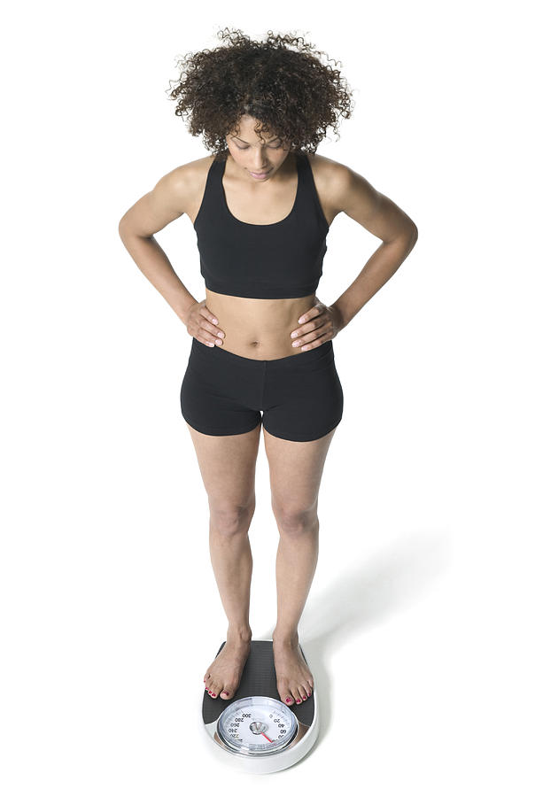High Angle Full Body Of A Young Adult Woman In A Black Workout Outfit As She Stands On The Scale Photograph by Photodisc