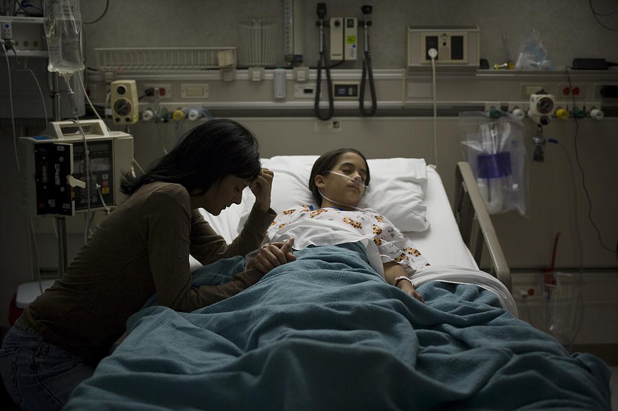 High angle view of a girl lying on a hospital bed with her mother holding her hand beside her Photograph by Rubberball