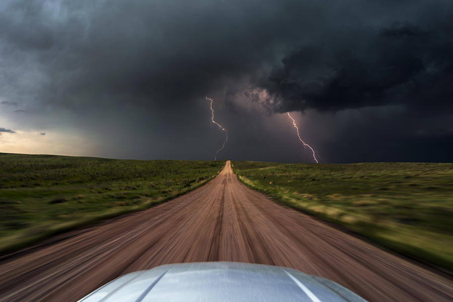 High speed storm chasing, taken from the roof of a moving car off road with double lightning bolts ahead. Colorado, USA. Photograph by John Finney Photography