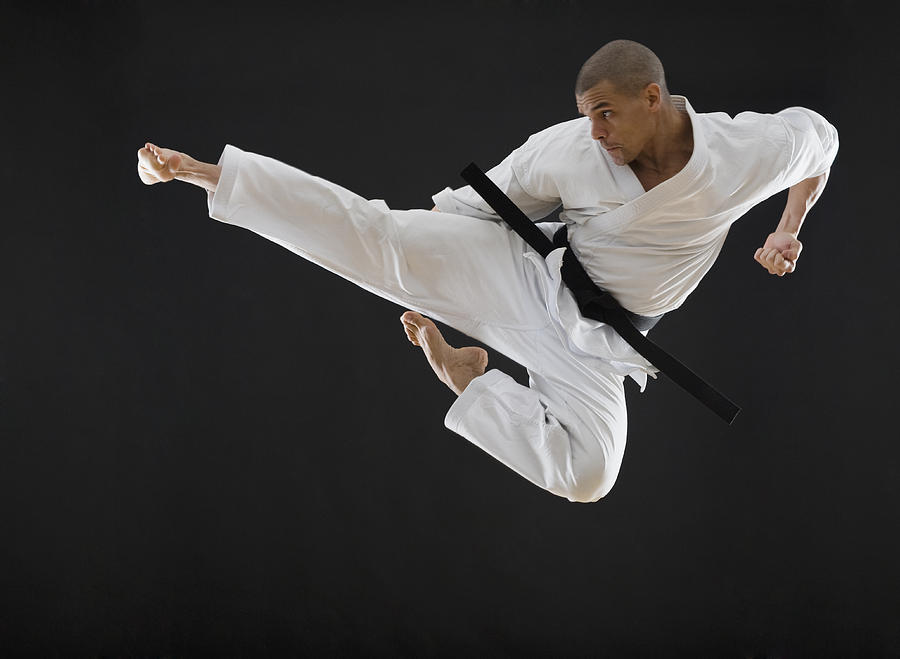 Hispanic male karate black belt kicking in air Photograph by Tetra Images